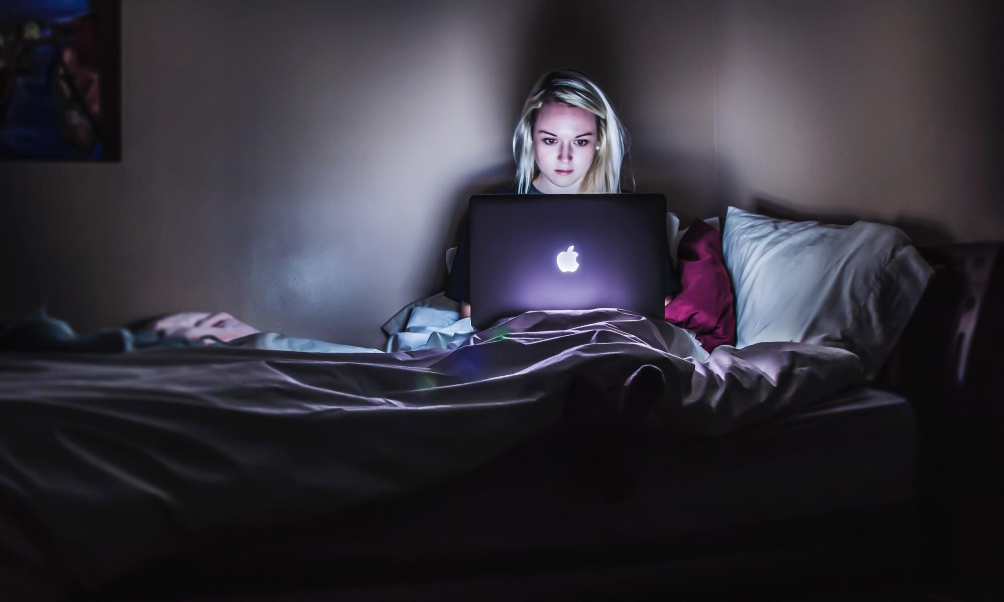 Frau sitzt mit Laptop im Bett